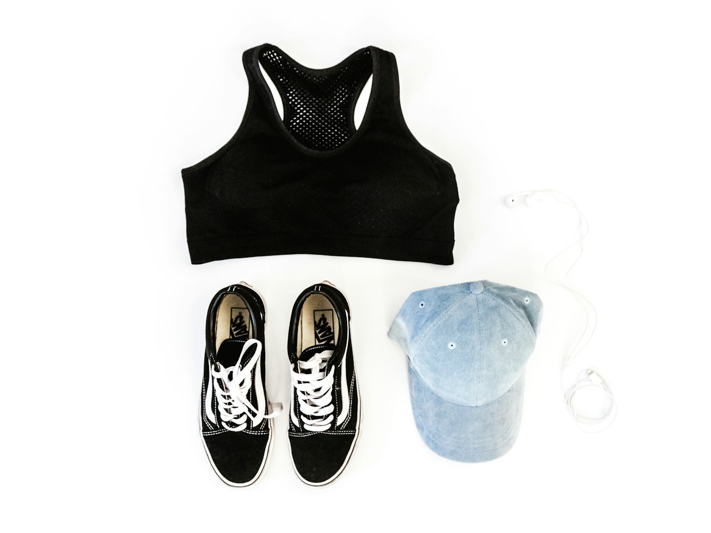 Black sports bra, sneakers, baseball cap, and earbuds arranged on white.