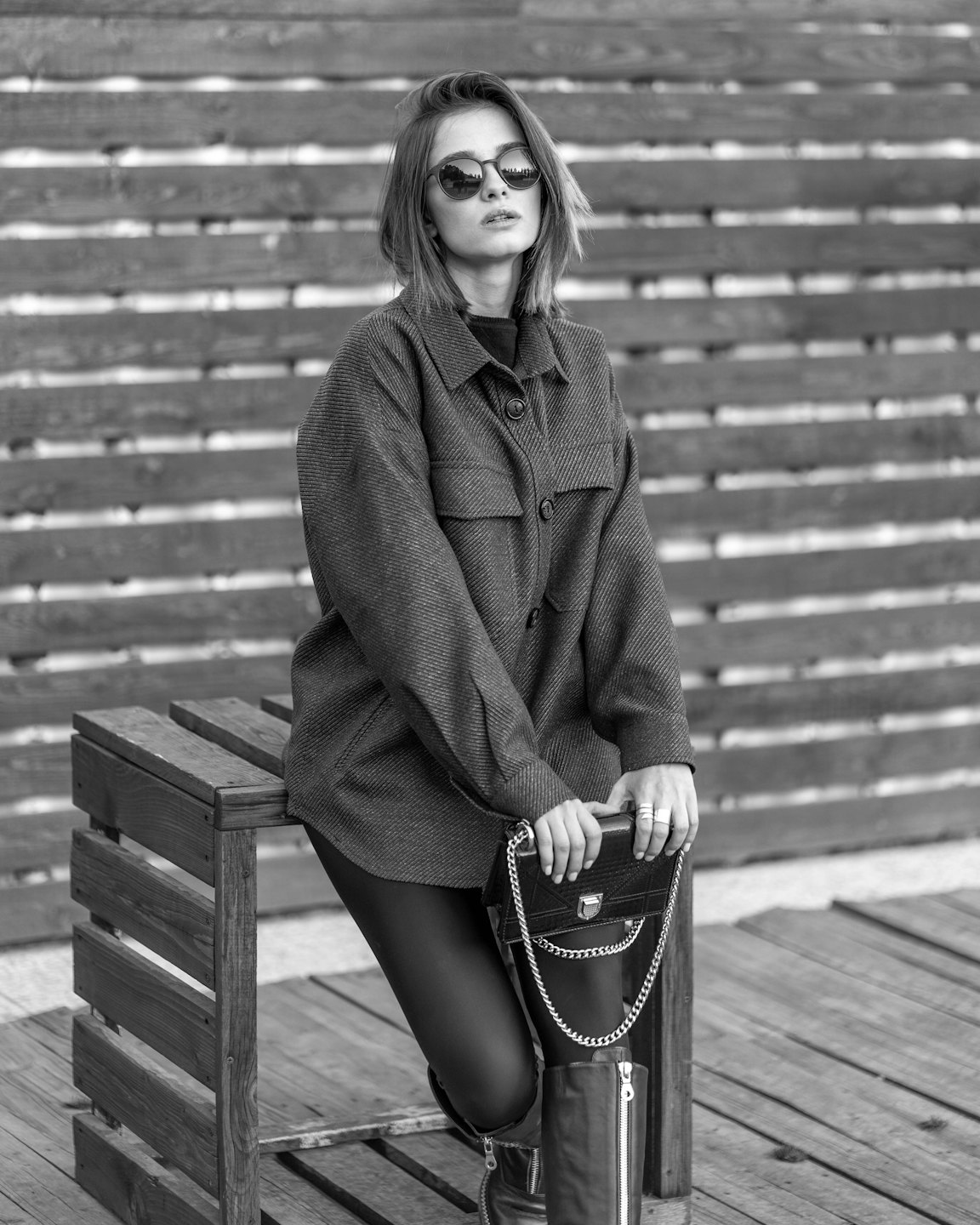 Woman in sunglasses leans against a rustic wooden bench.