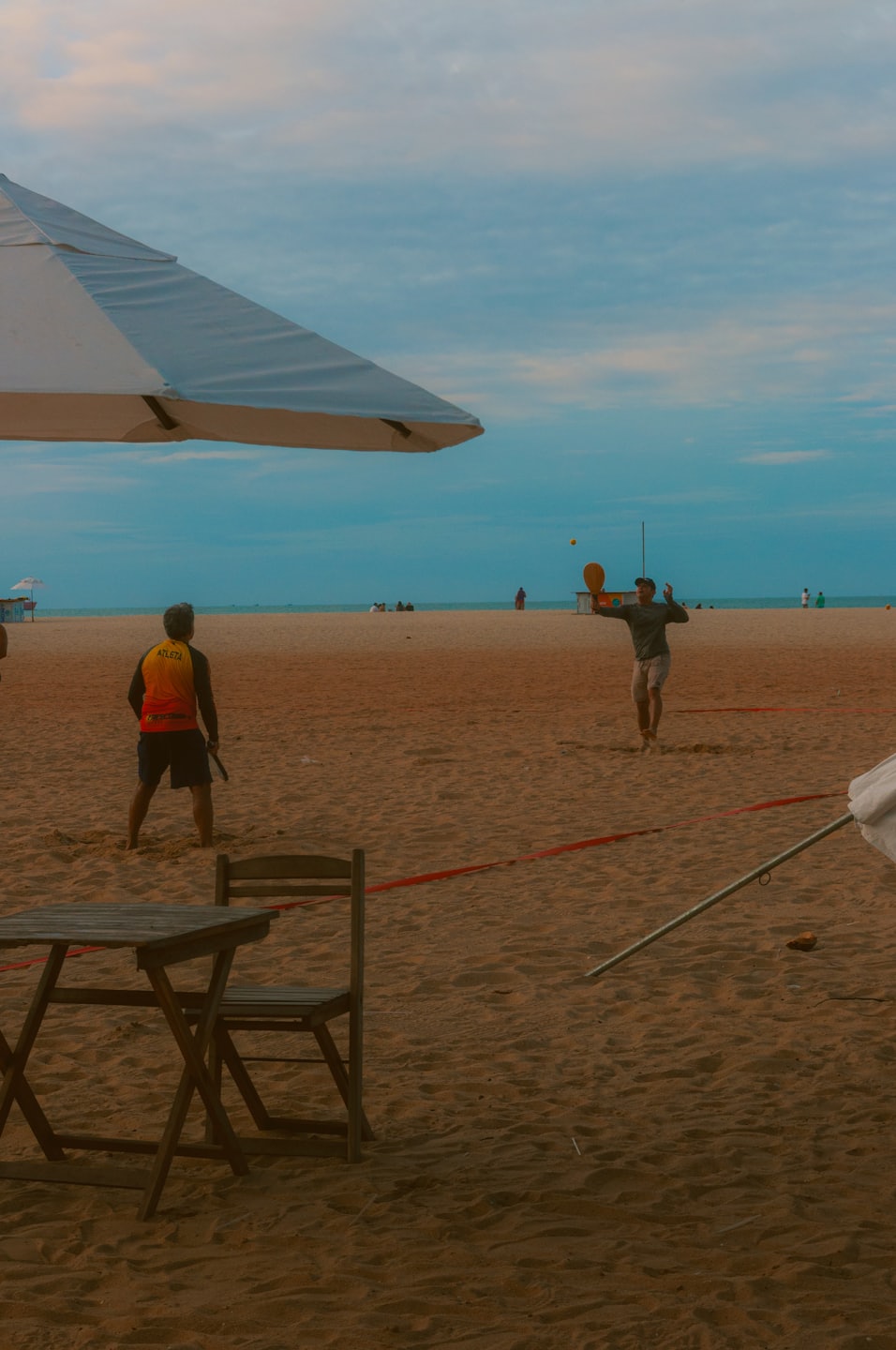 Two men play beach tennis on a sandy shore.