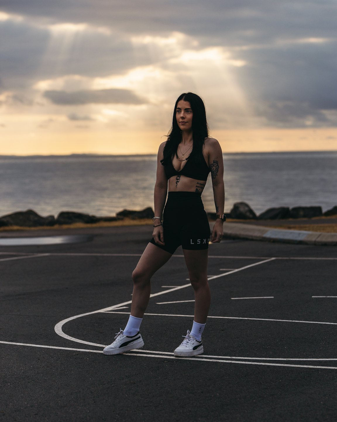Woman in athletic wear poses by water on a court.