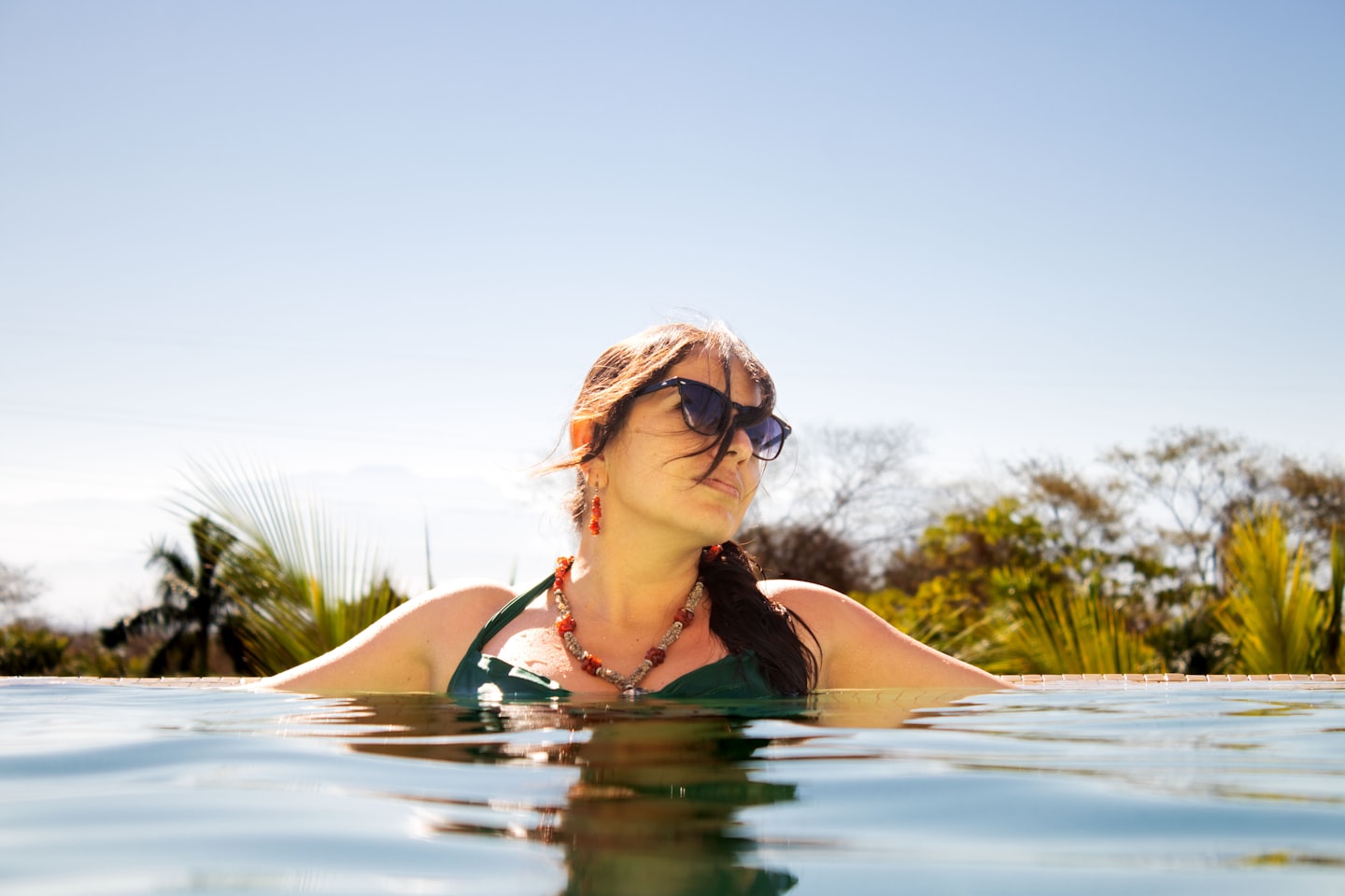 Woman in a green swimsuit relaxing in an infinity pool.